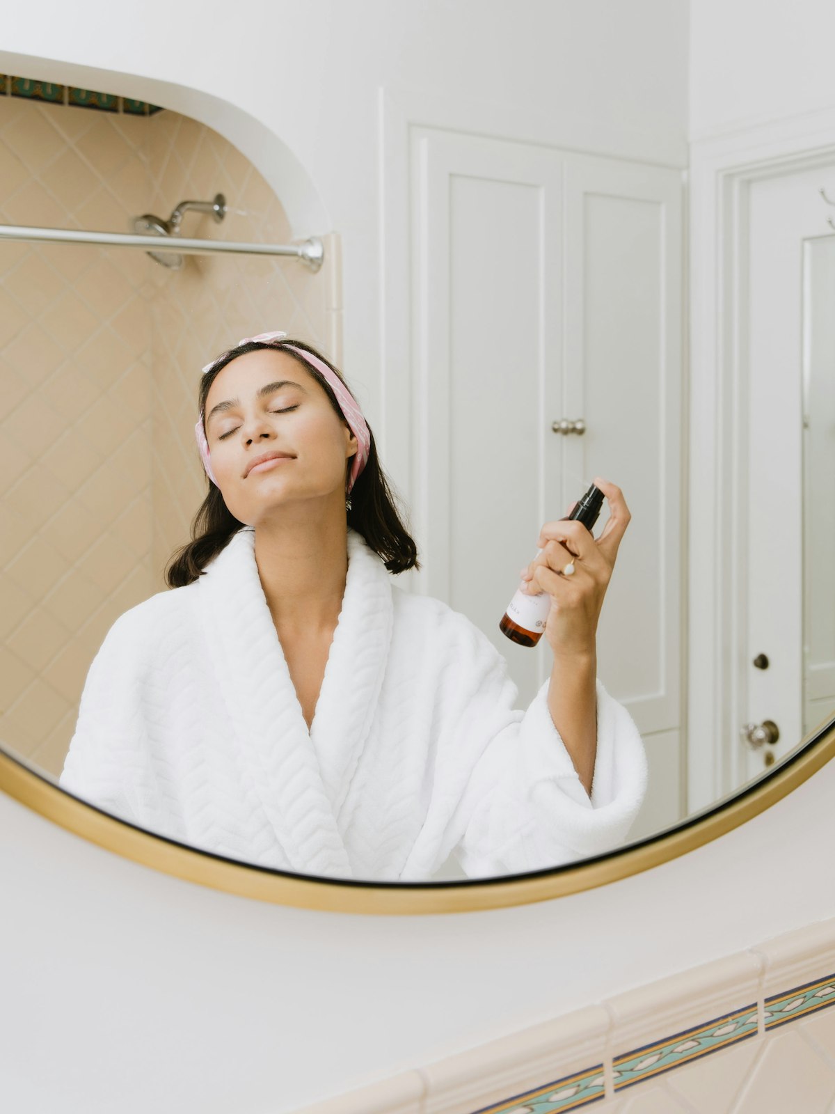 Woman closing her eyes and misting setting spray over her finished makeup before an evening out