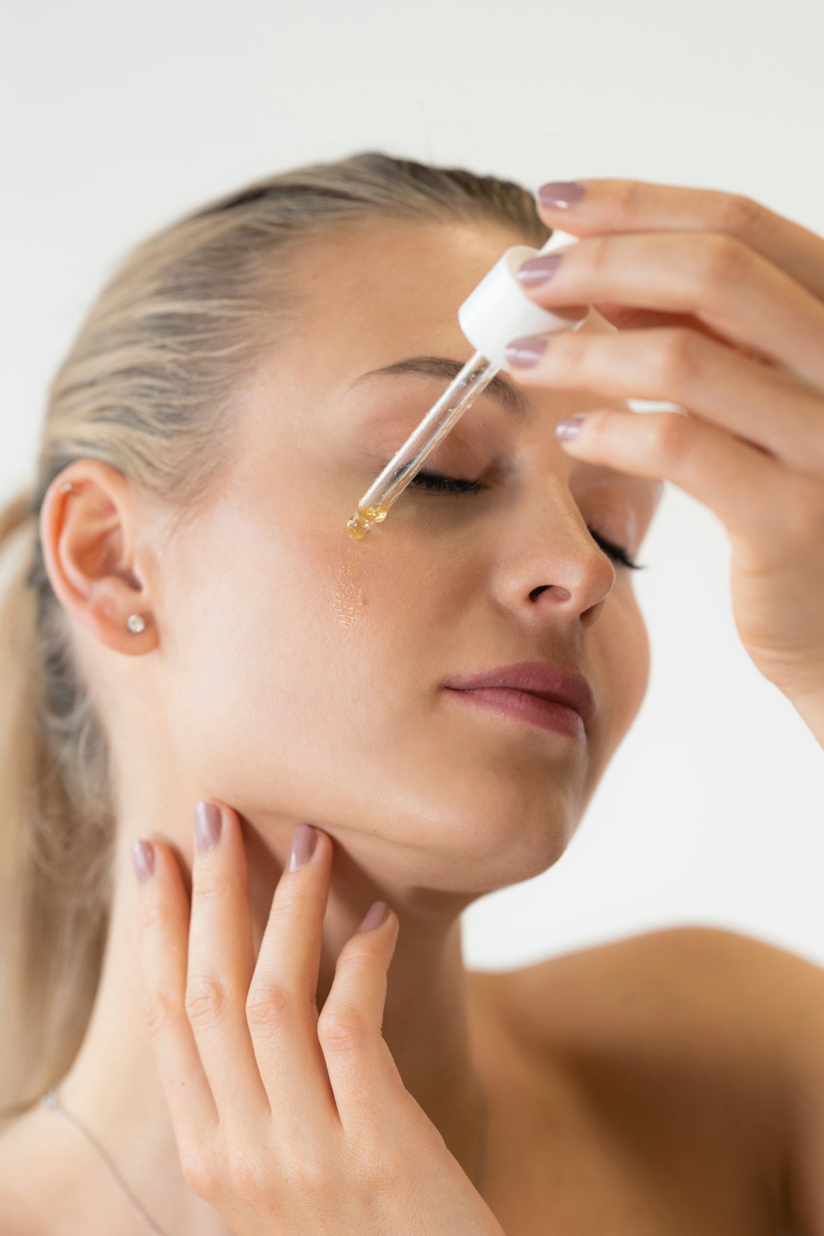 Woman applying serum at her bathroom mirror in soft morning light, skincare bottles lined up beside the sink