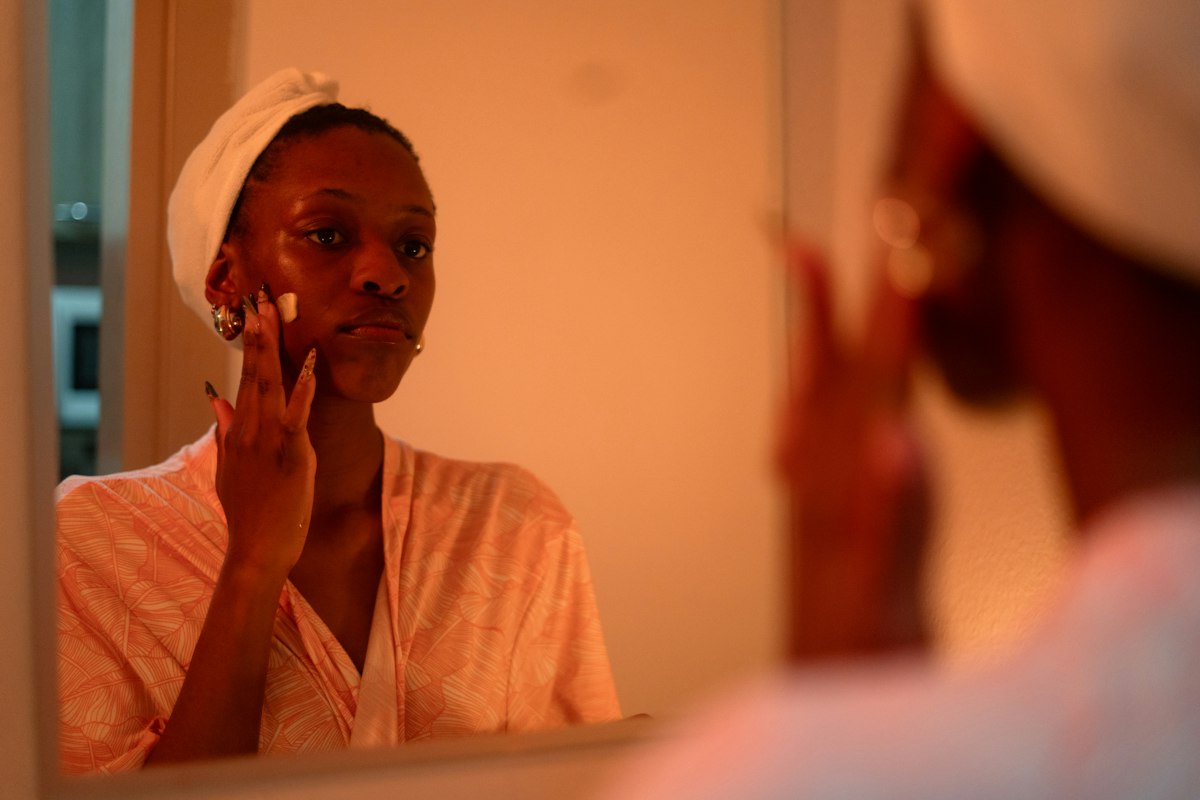 Evening skincare routine on a bedroom vanity, woman patting moisturizer onto her face before bed