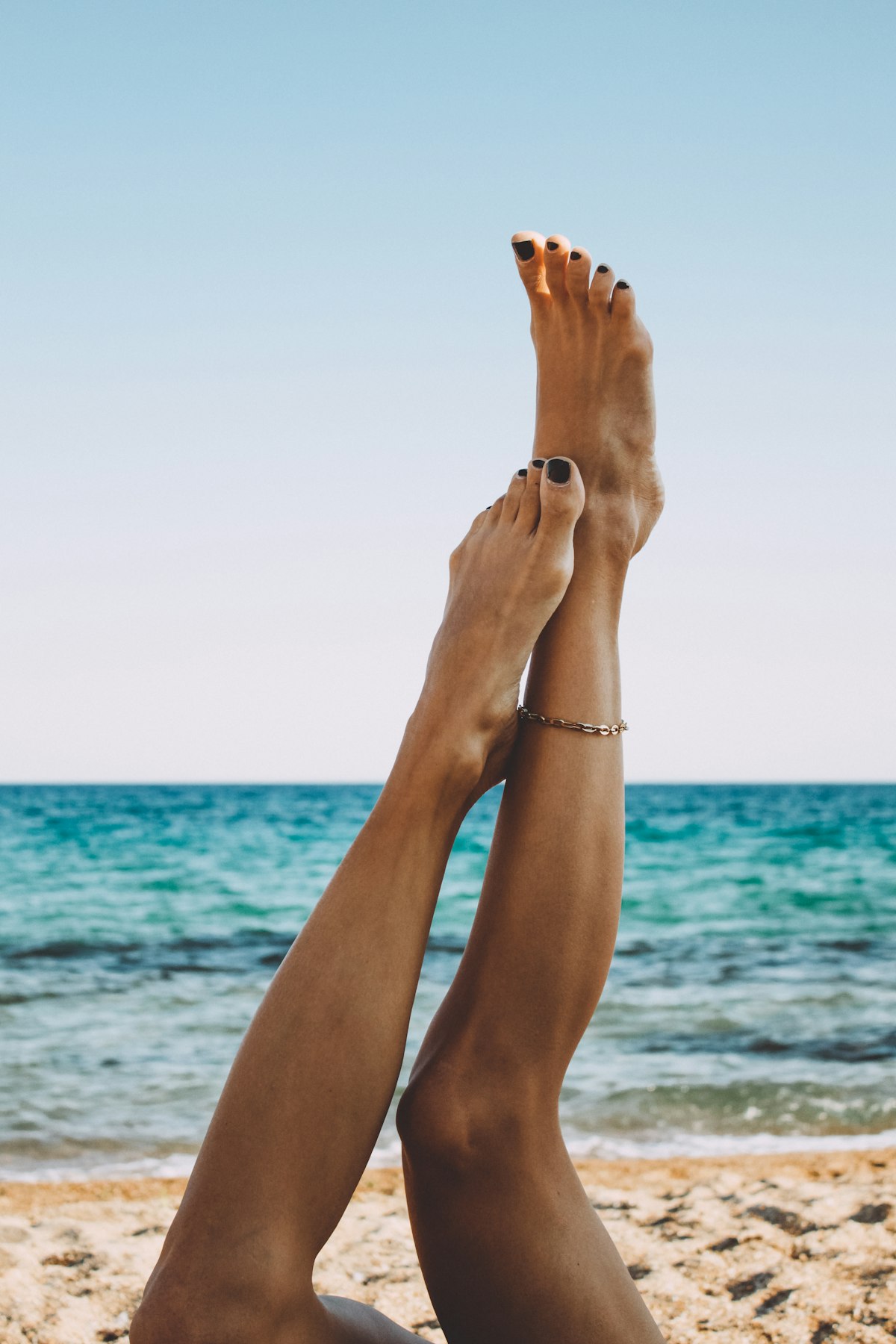 Woman applying self-tanner with a mitt to her legs in a sunlit bathroom before vacation